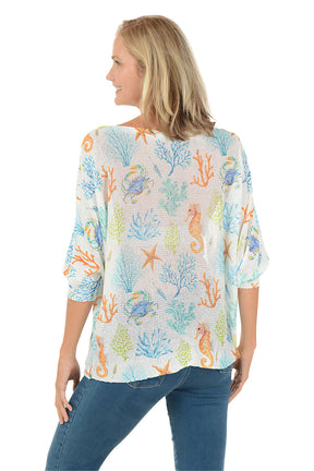 Woman wearing a colorful marine-themed shirt with seahorses and coral on a white background. Back shot.