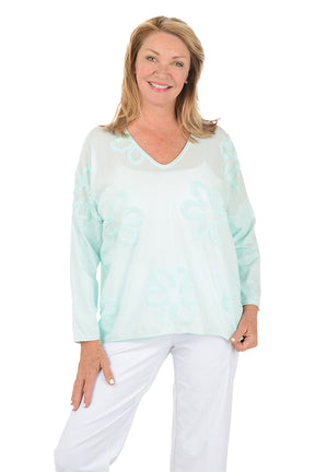 Woman wearing a light blue floral blouse and white pants on a white background.