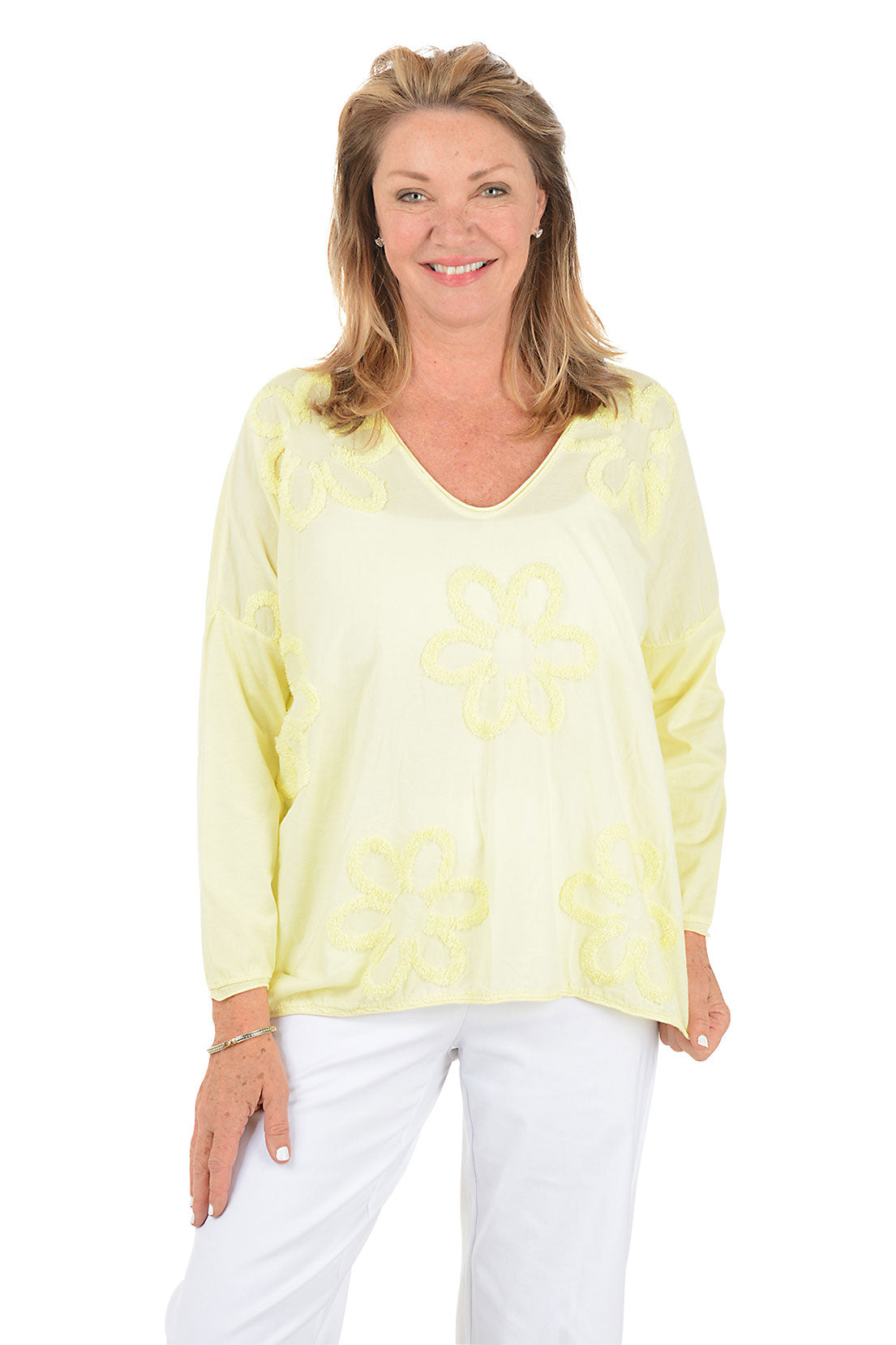 Woman wearing a light yellow floral blouse and white pants on a white background.