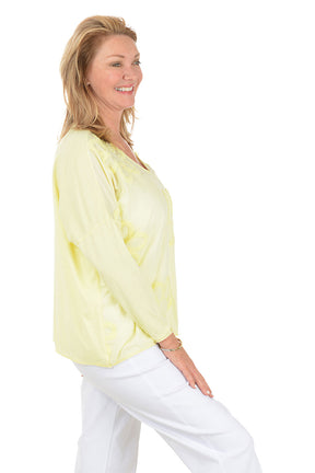 Woman wearing a light yellow floral blouse and white pants on a white background. Side shot.