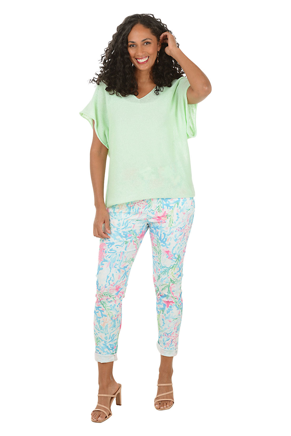 Woman wearing a light green top and floral pants on a white background.