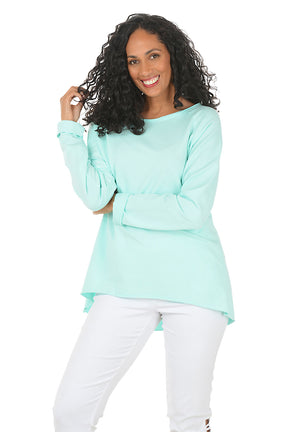 Woman wearing a light blue long-sleeve top and white pants on a white background.