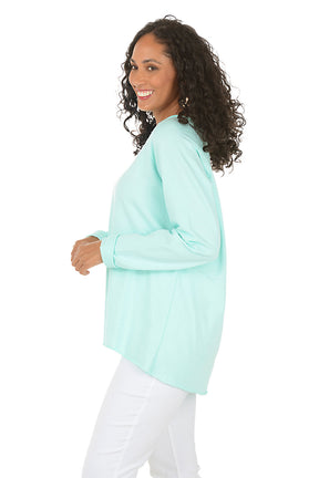 Woman wearing a light blue long-sleeve top and white pants on a white background. Side shot.