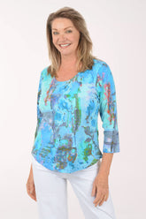 Woman wearing a colorful patterned top and white pants on a white background
