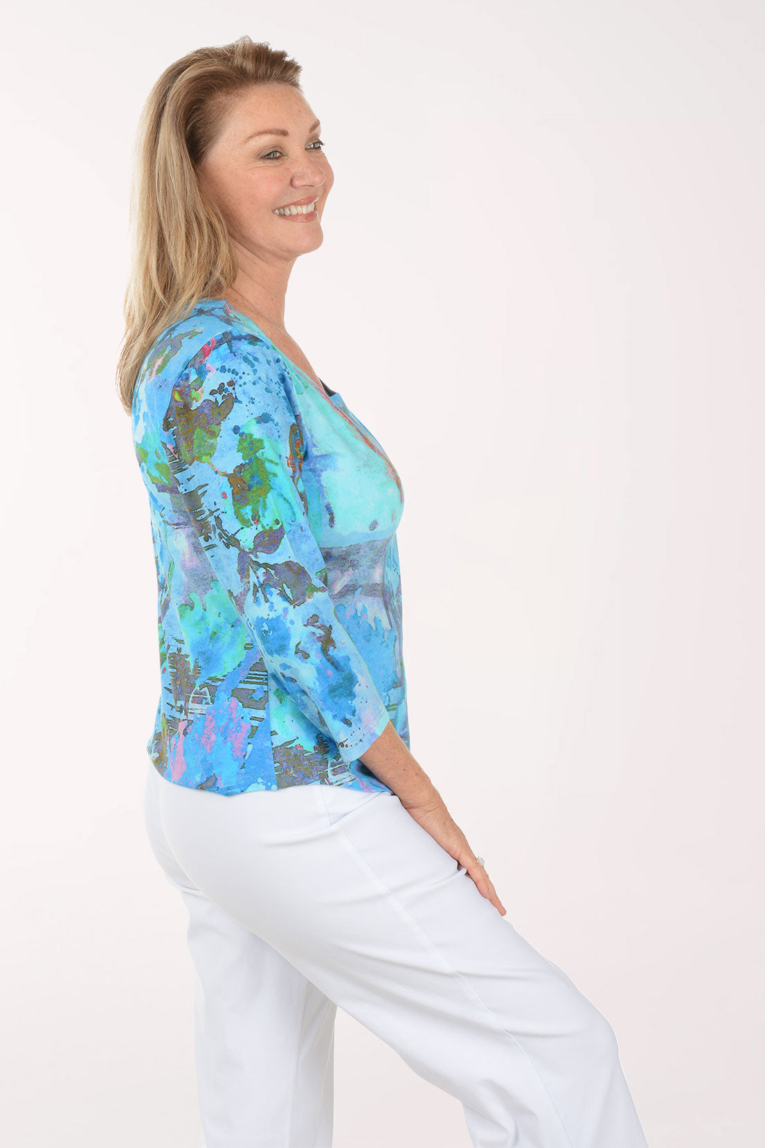 Woman wearing a colorful patterned top and white pants on a white background