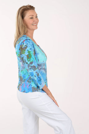 Woman wearing a colorful patterned top and white pants on a white background