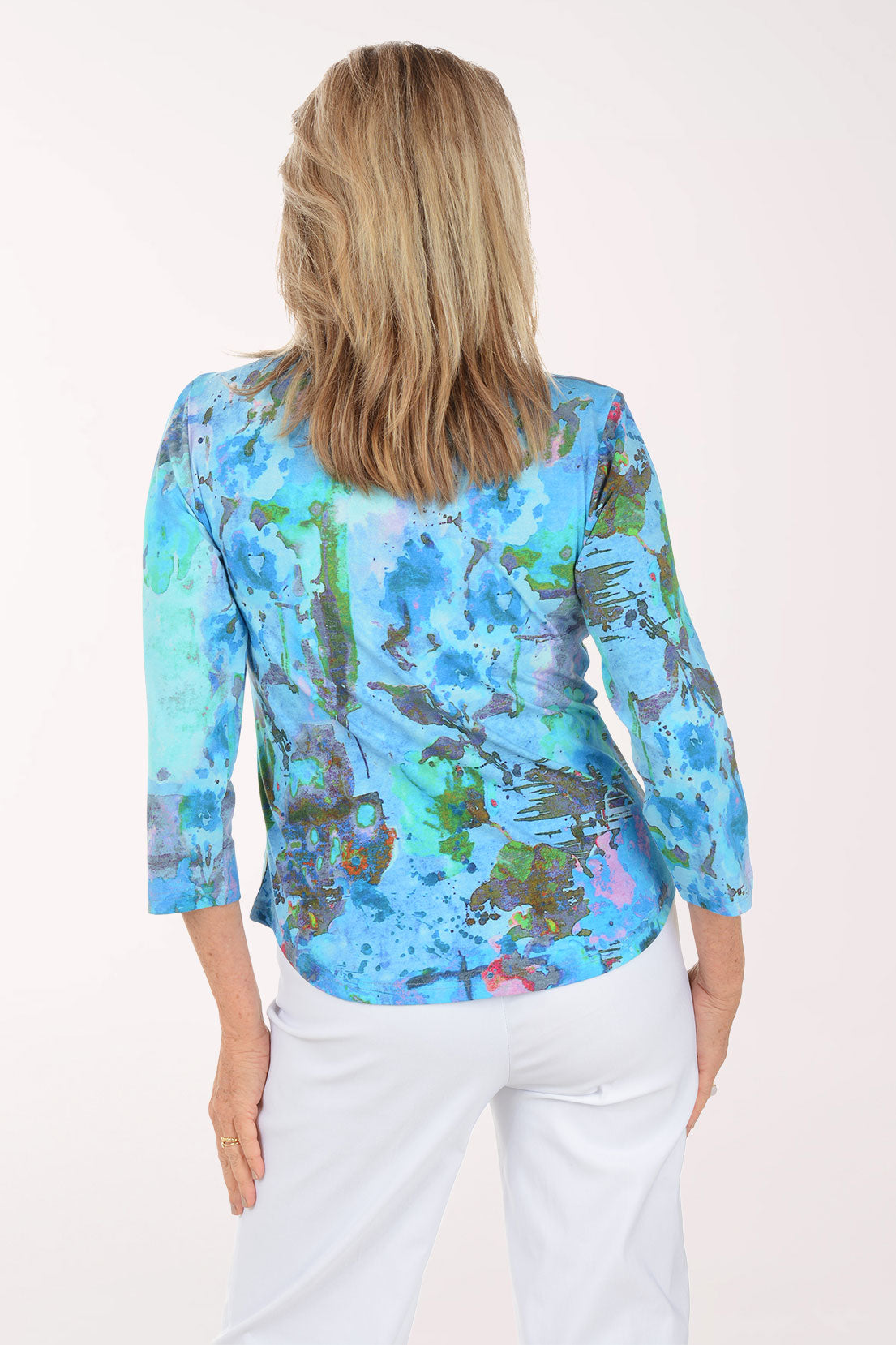 Woman wearing a colorful patterned top and white pants on a white background