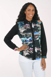 A woman modeling a long-sleeve button-up shirt with black sleeves and a colorful abstract collage print on the front panel, paired with white pants against a plain white background.
