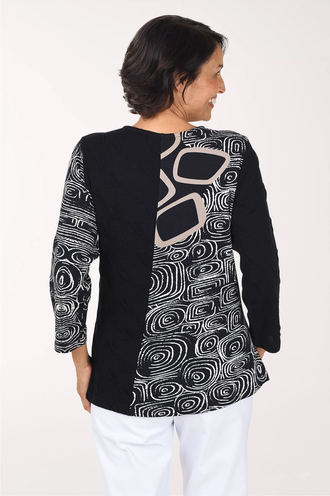 Woman wearing a 3/4 sleeve black top with an abstract pattern on half of the top, one arm, and pocket.