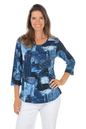 Woman wearing a 3/4 sleeve blue patterned top with white pants on a white background.