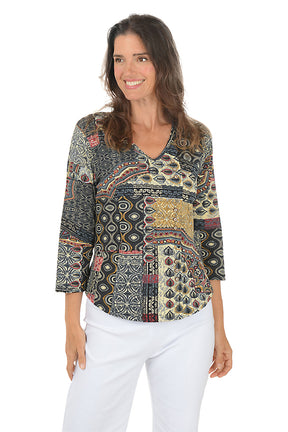 Woman wearing a 3/4 sleeve paisley patterned blouse and white pants on a white background.