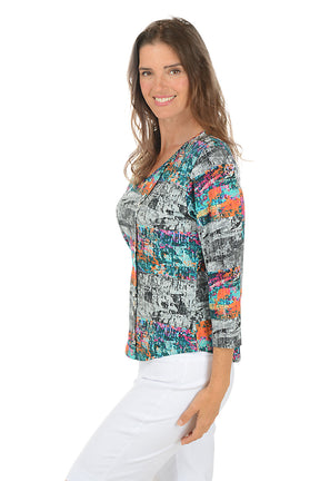 Woman wearing a colorful abstract patterned blouse with white pants on a white background. Side shot.