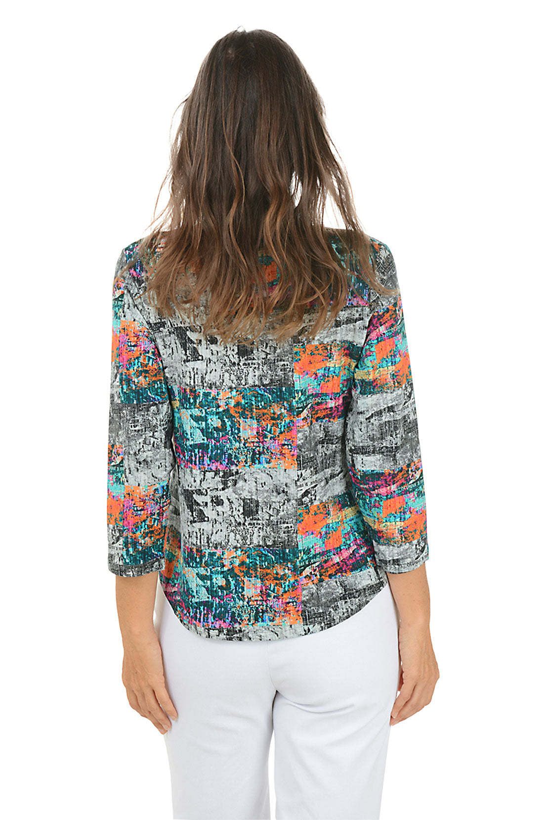 Woman wearing a colorful abstract patterned blouse with white pants on a white background. Back shot.
