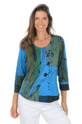 Woman wearing a colorful patterned top with blue and green design on a white background.