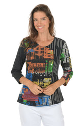 Woman wearing a 3/4 sleeve colorful typesetting patterned top with a white background.
