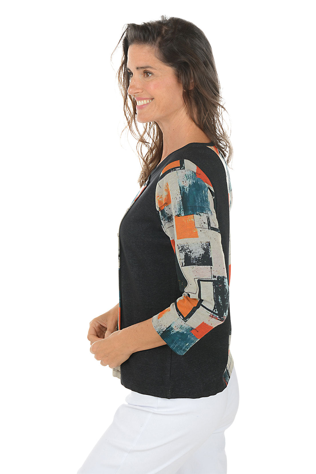 Woman wearing a 3/4 sleeve black and multicolor abstract patterned top with white pants on a white background. Side shot.