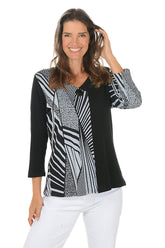 Woman wearing a black and white patterned blouse with white pants on a white background.