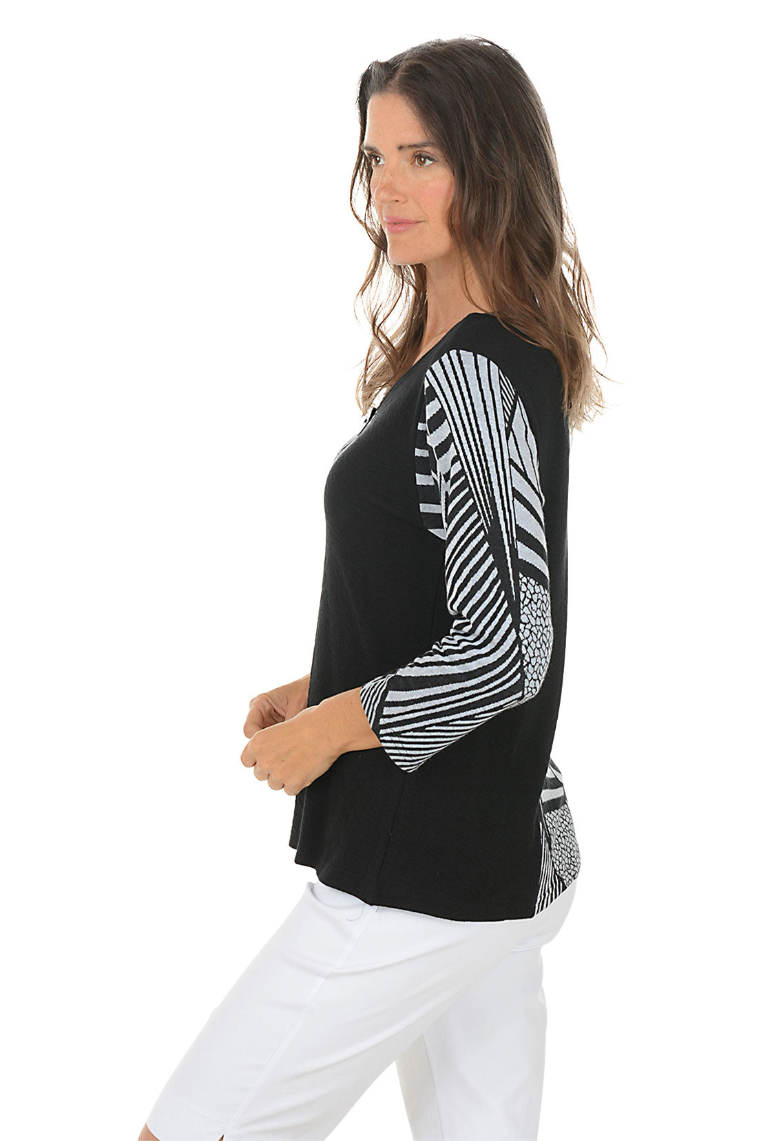Woman wearing a black and white patterned blouse with a white background. Side shot.