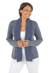 Woman wearing a blue knitted cardigan over a white top on a white background.