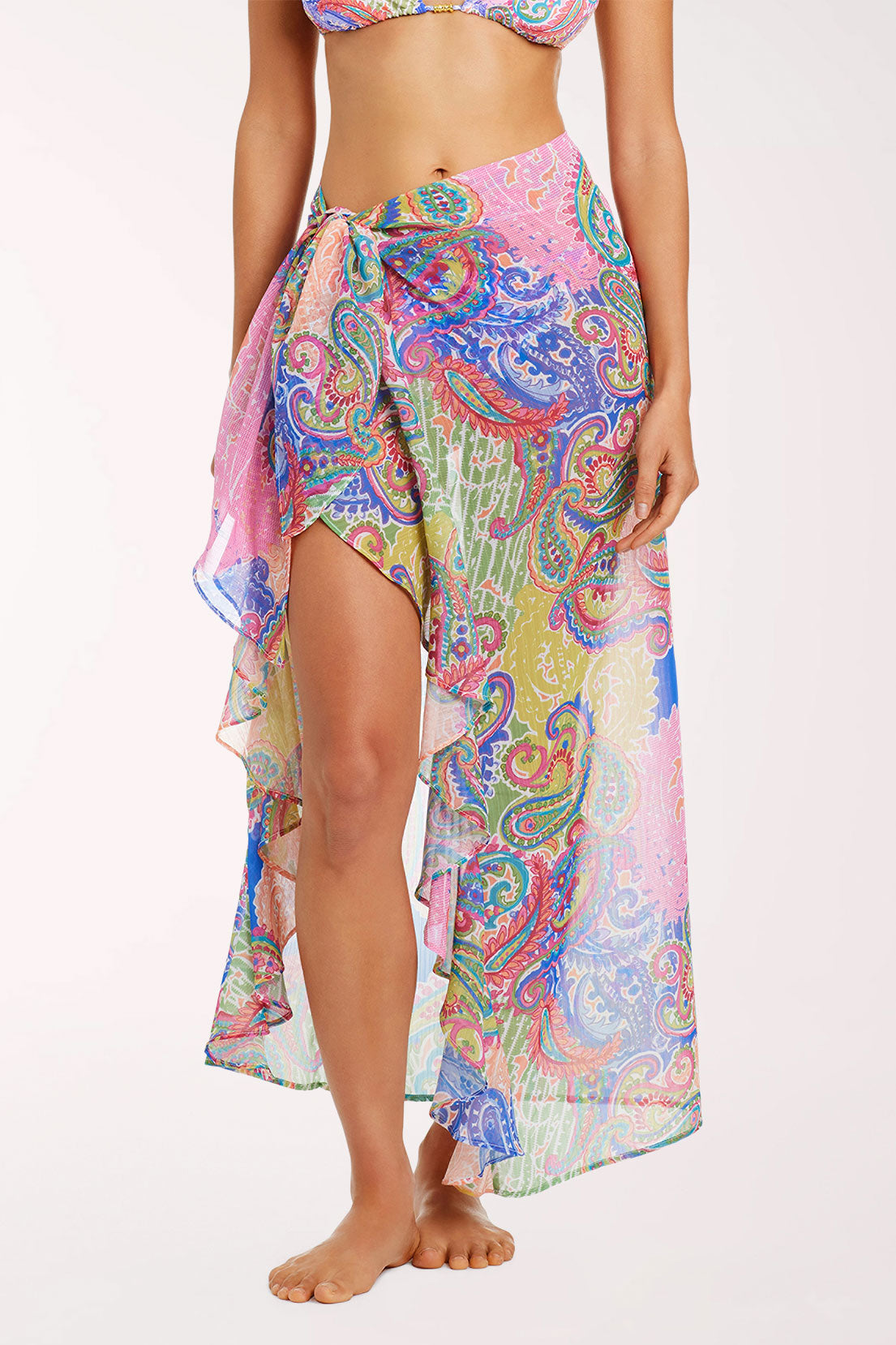 Front view of a woman wearing the La Vida Bohemia Ruffled Chiffon Sarong, a semi-sheer paisley patchwork print in pink, lavender, lime green, coral and cobalt blue, tied at the hip with ruffled edges and an asymmetric hem falling to the lower calf, over a matching bikini.