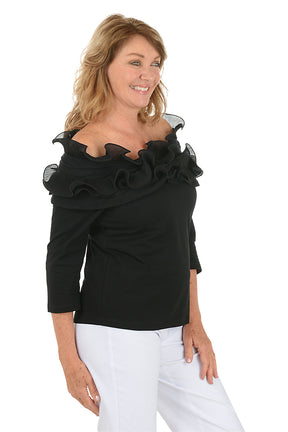 Woman wearing a black off-shoulder top with ruffles on a white background. Side shot.