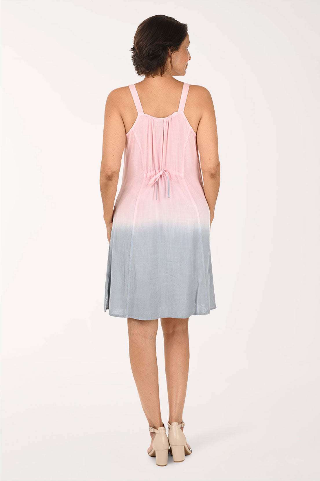 A woman modeling a sleeveless A-line dress with a pink and light blue ombre gradient, featuring a lace-up neckline and embroidered palm trees near the hem.