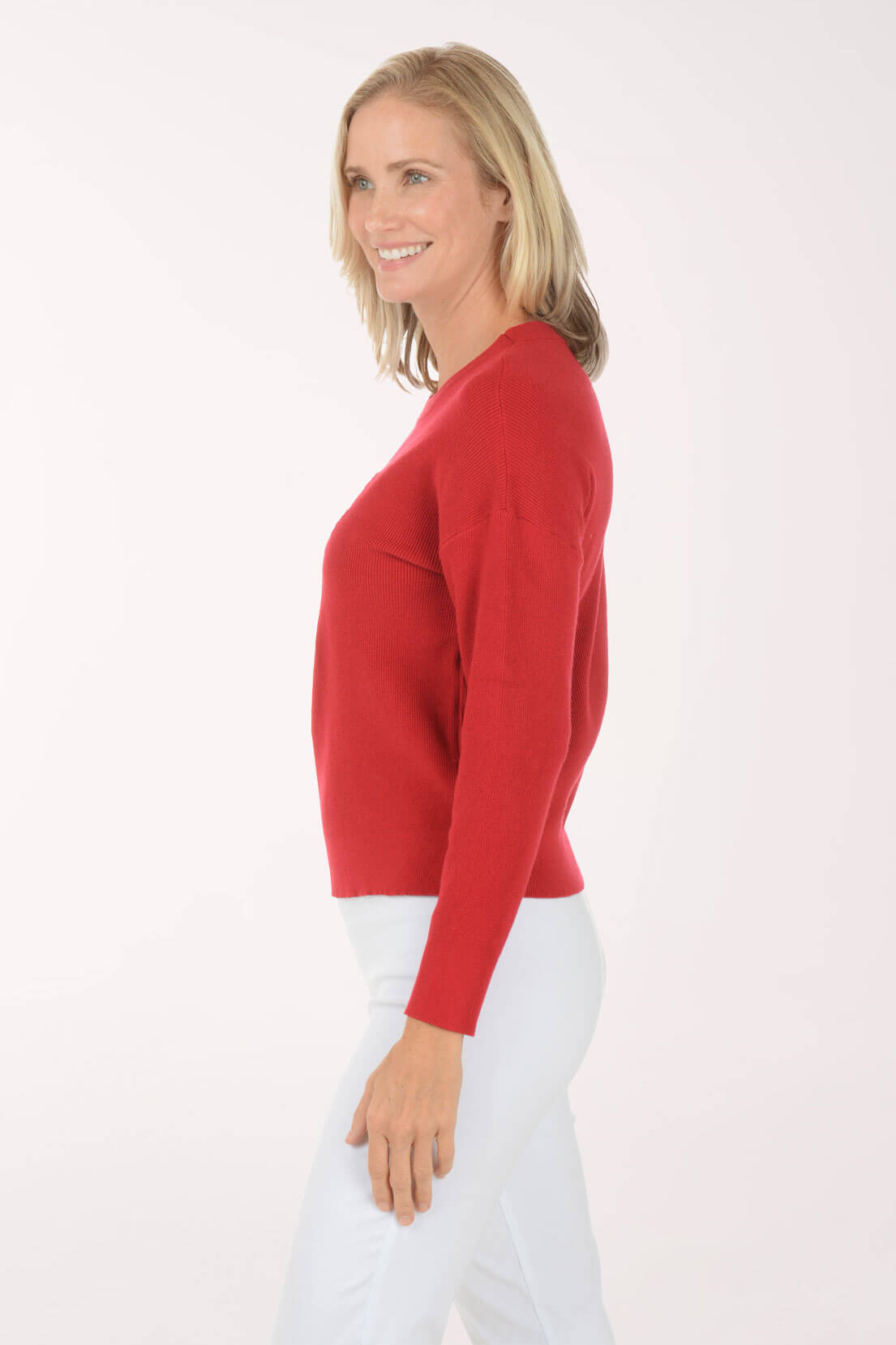 Woman wearing a red sweater and white pants on a white background. Side shot.