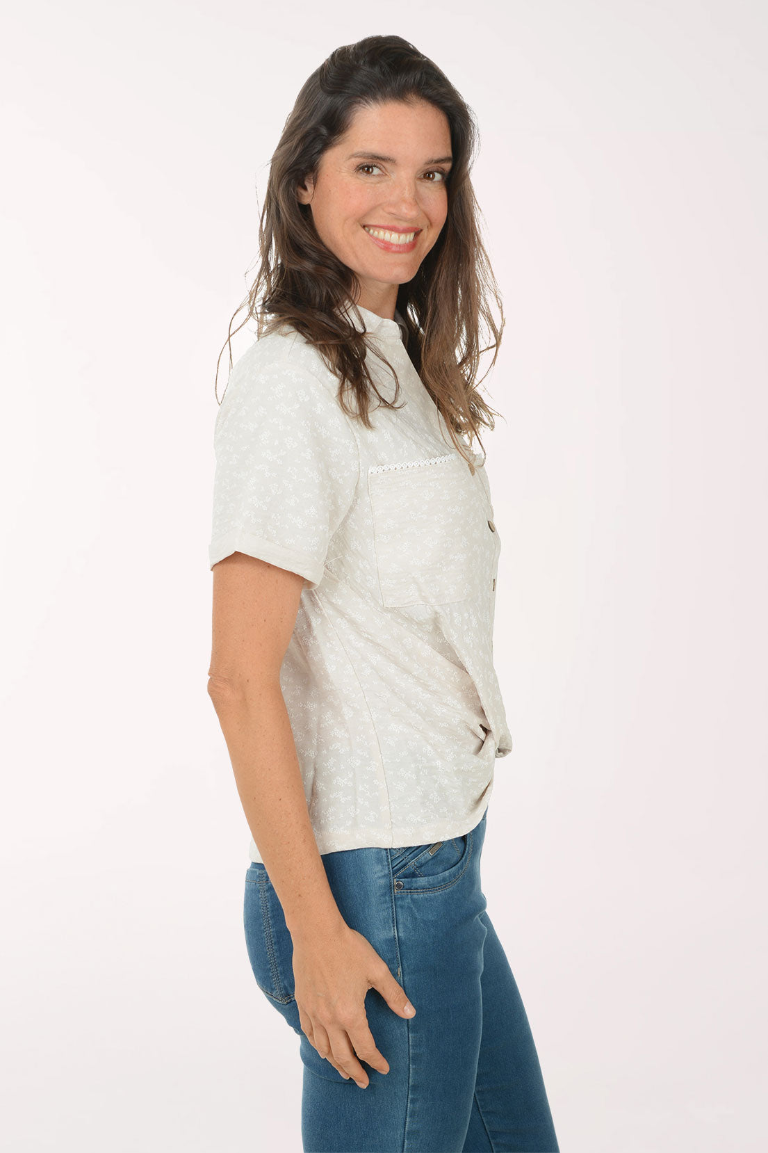 Woman wearing a beige patterned shirt and blue jeans on a white background