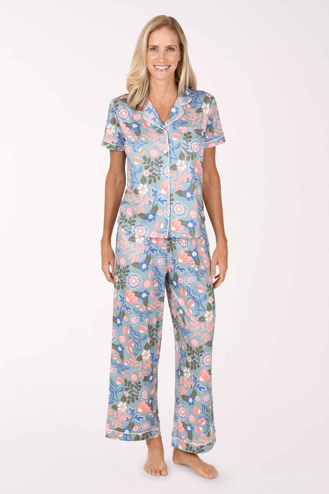 A woman modeling a two-piece short-sleeve pajama set with a blue, pink, and green floral pattern against a plain white studio background.