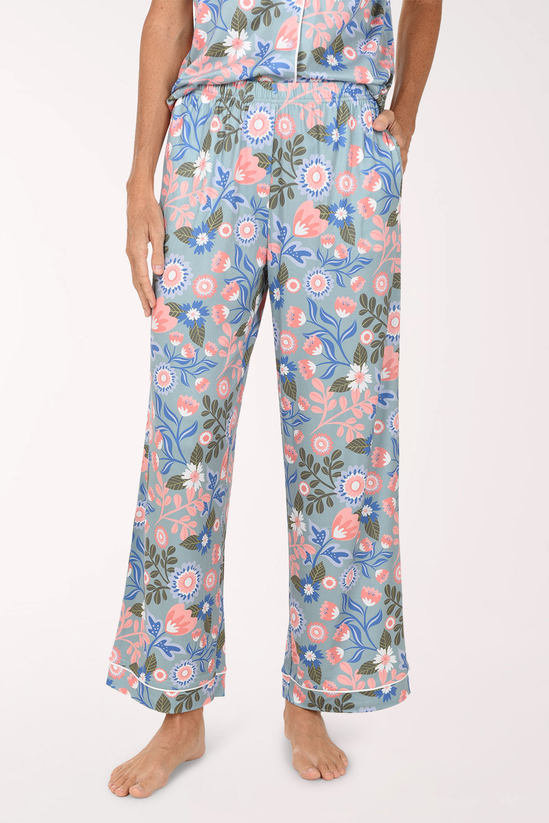 A person wearing a matching floral pajama set with light blue pants featuring pink, peach, and green botanical prints, shown against a plain light background.