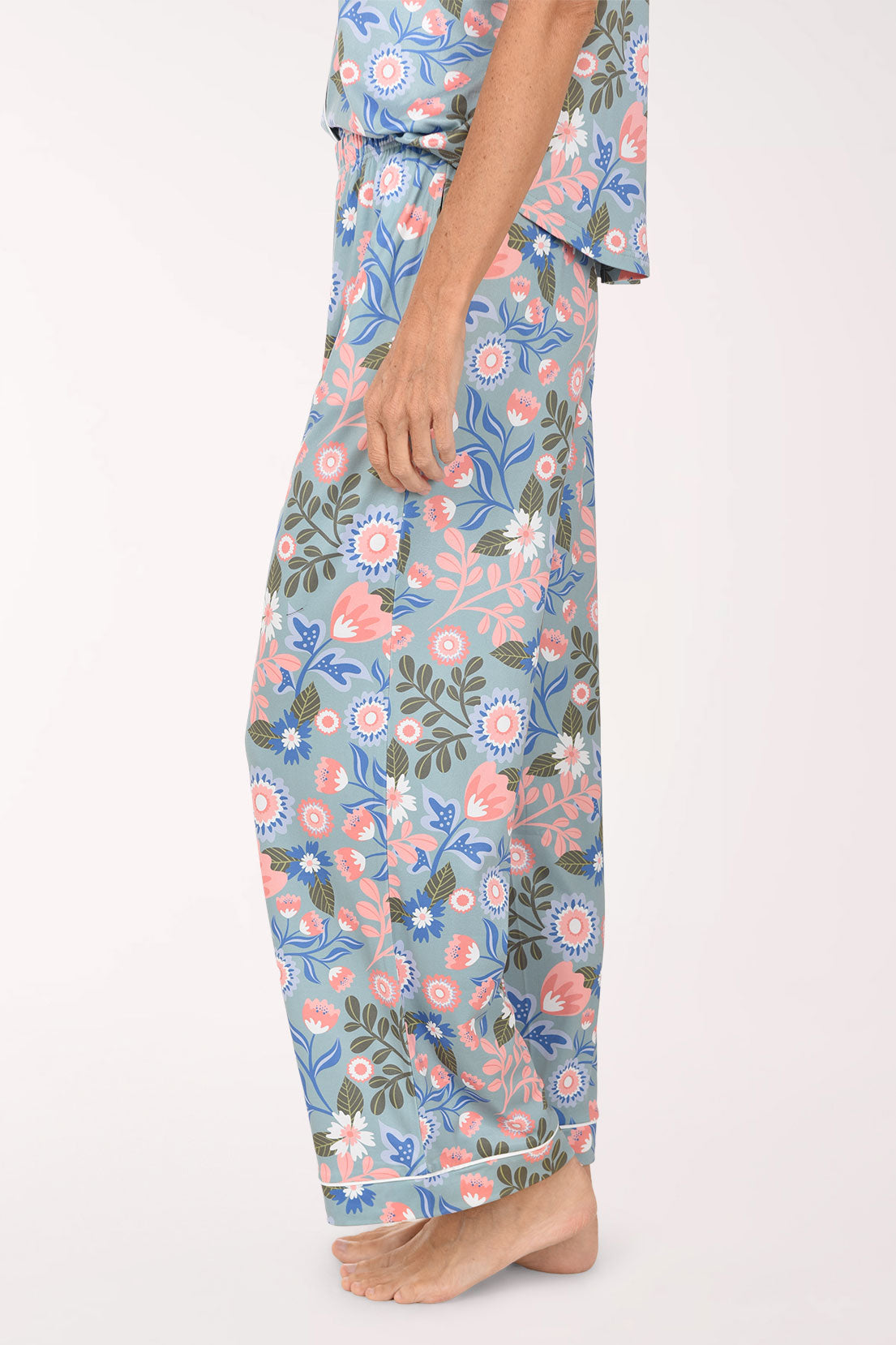 A person wearing a matching floral pajama set with light blue pants featuring pink, peach, and green botanical prints, shown against a plain light background.