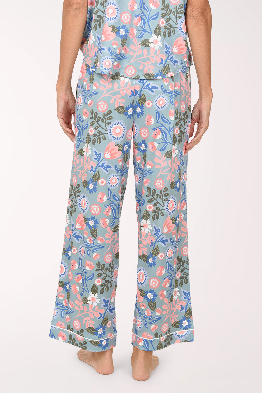 A person wearing a matching floral pajama set with light blue pants featuring pink, peach, and green botanical prints, shown against a plain light background.
