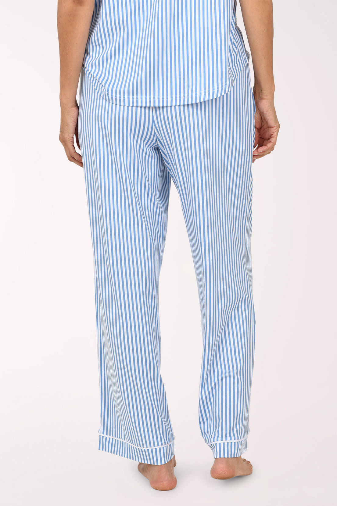 A person shown from the back wearing light blue and white vertically striped pajama pants and a matching top against a plain light background.