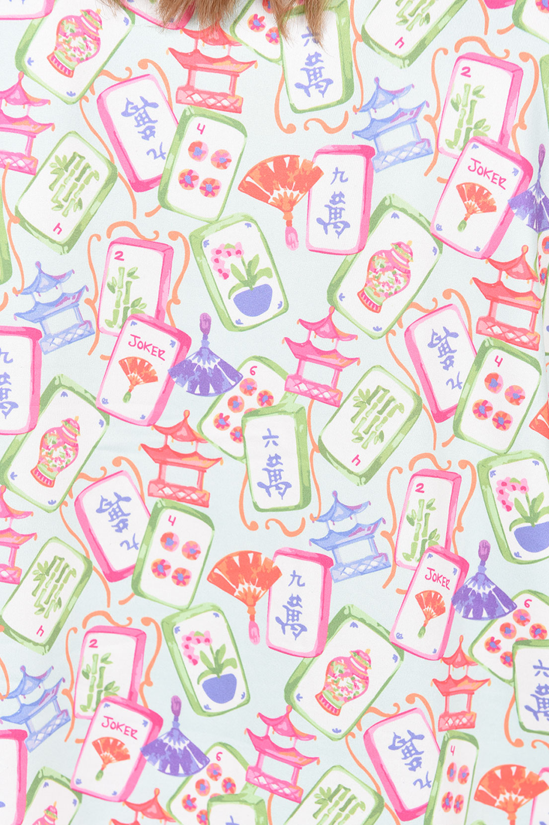 A close-up of a white fabric featuring a colorful repeating pattern of Japanese mahjong tiles, including pink, green, and purple illustrations of tiles, fans, pagoda towers, and kanji characters.