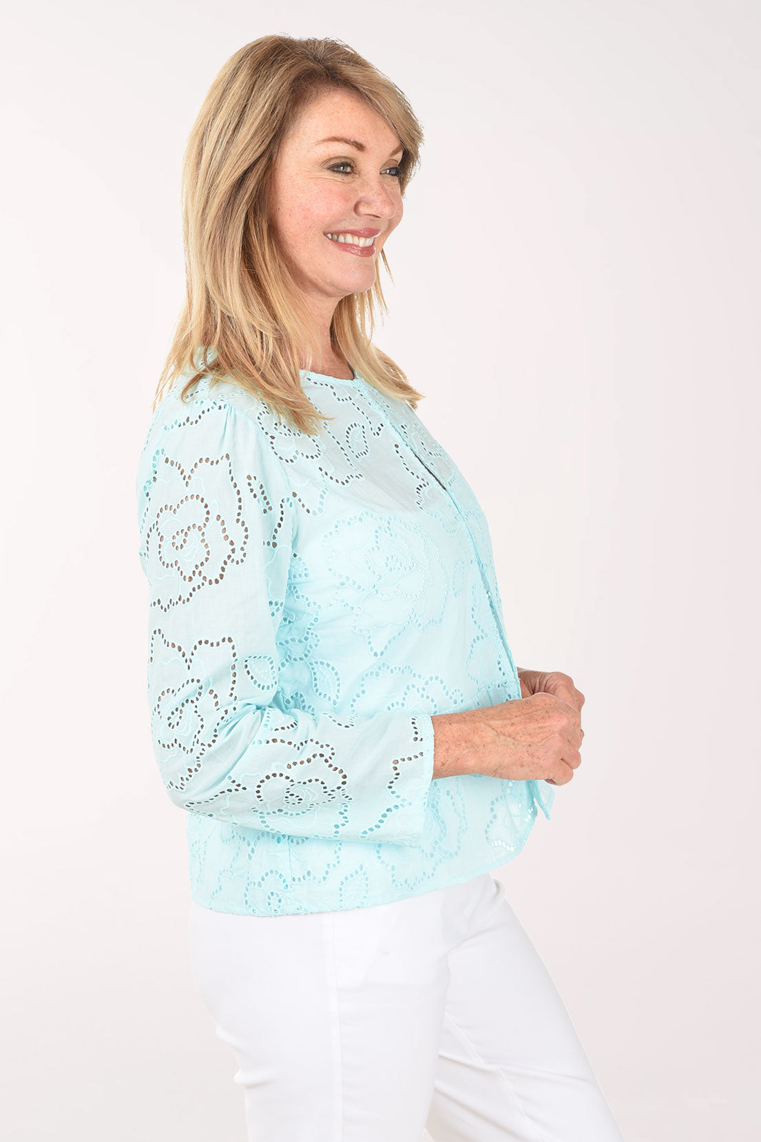 Woman wearing a light blue lace top and white pants on a white background