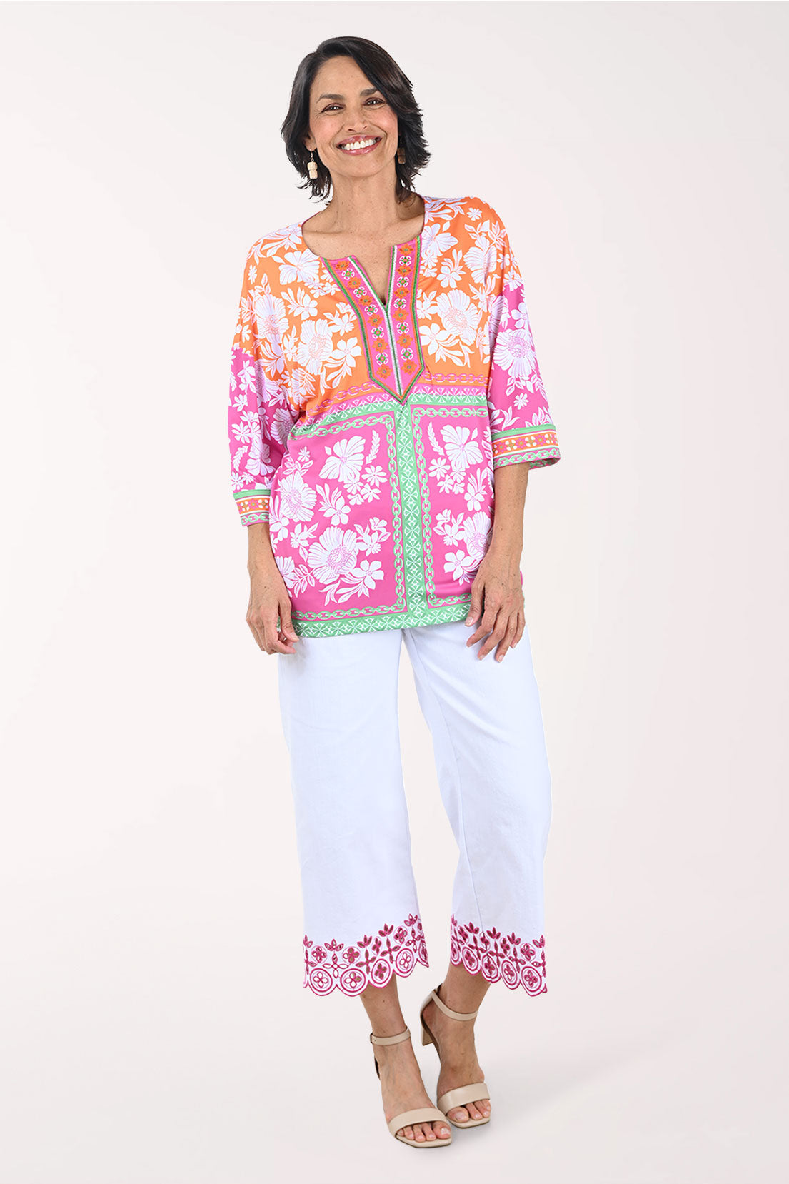 Woman wearing a colorful embroidered top and white pants on a white background