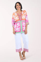 Woman wearing a colorful embroidered top and white pants on a white background