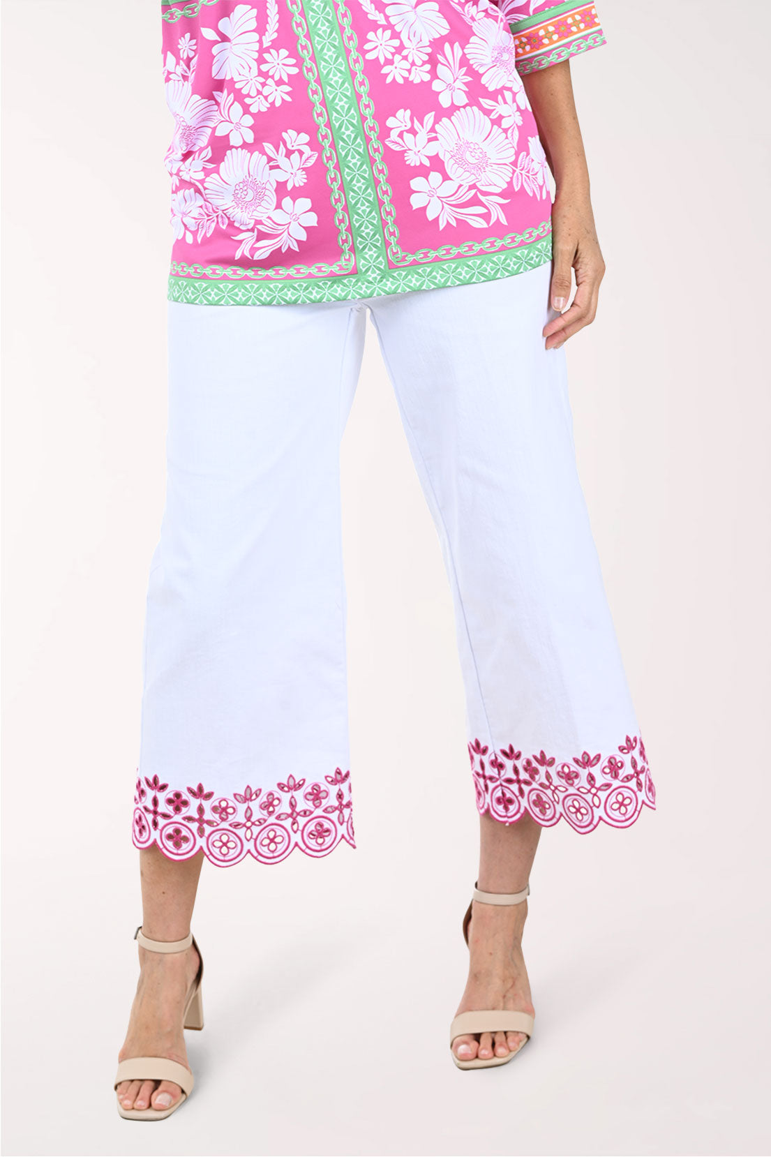 Woman wearing a pink floral top and white pants with pink embroidery on a white background