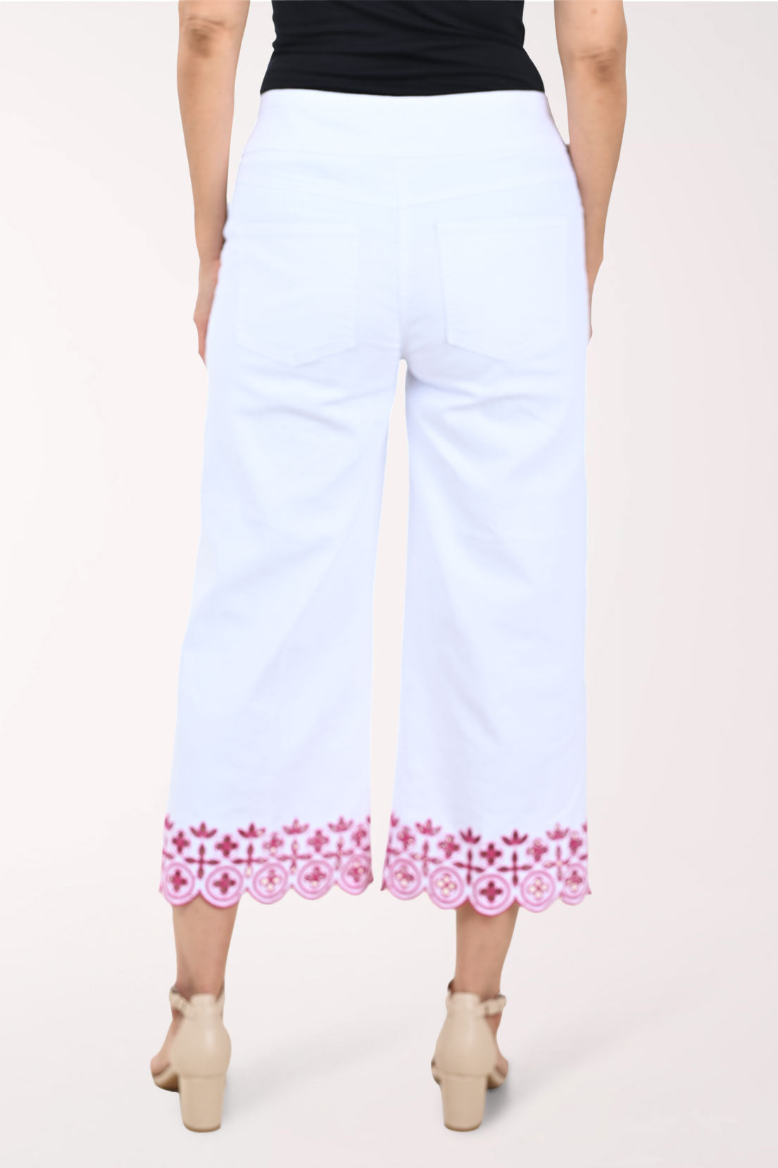 White pants with pink floral embroidery worn by a person on a white background