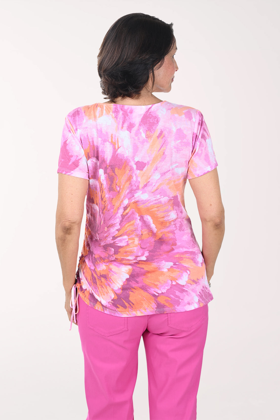 Woman wearing a pink and orange tie-dye shirt with pink pants on a white background