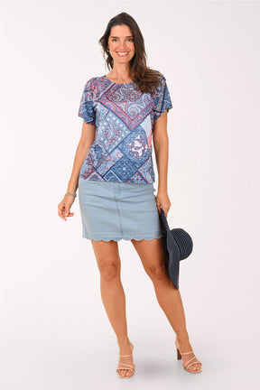 Woman wearing a patterned top and denim skirt holding a hat on a white background