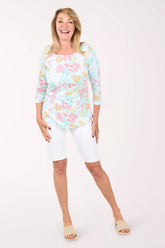 Woman wearing a floral top and white capri pants on a white background