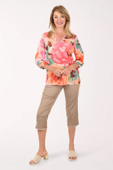 Woman wearing a colorful floral blouse and beige pants on a white background