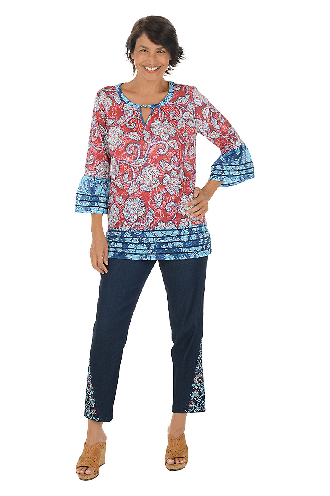 Woman wearing a colorful patterned top and navy pants on a white background.