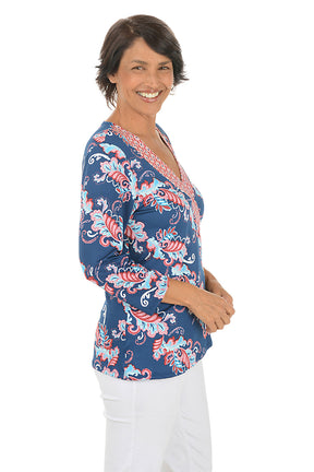 Woman wearing a colorful patterned blouse with a white background. Side shot.