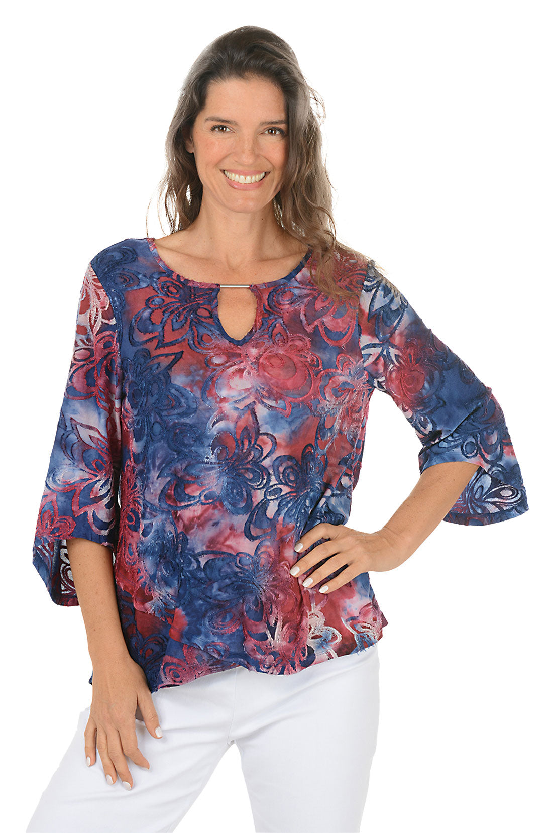 Woman wearing a colorful red and blue floral blouse with white pants on a white background.