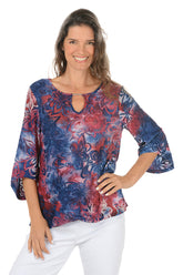 Woman wearing a colorful red and blue floral blouse with white pants on a white background.