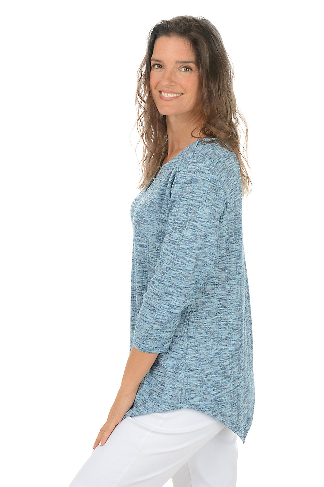 Woman wearing a blue knit top with an asymmetrical handkerchief hemline on white background. Side shot.
