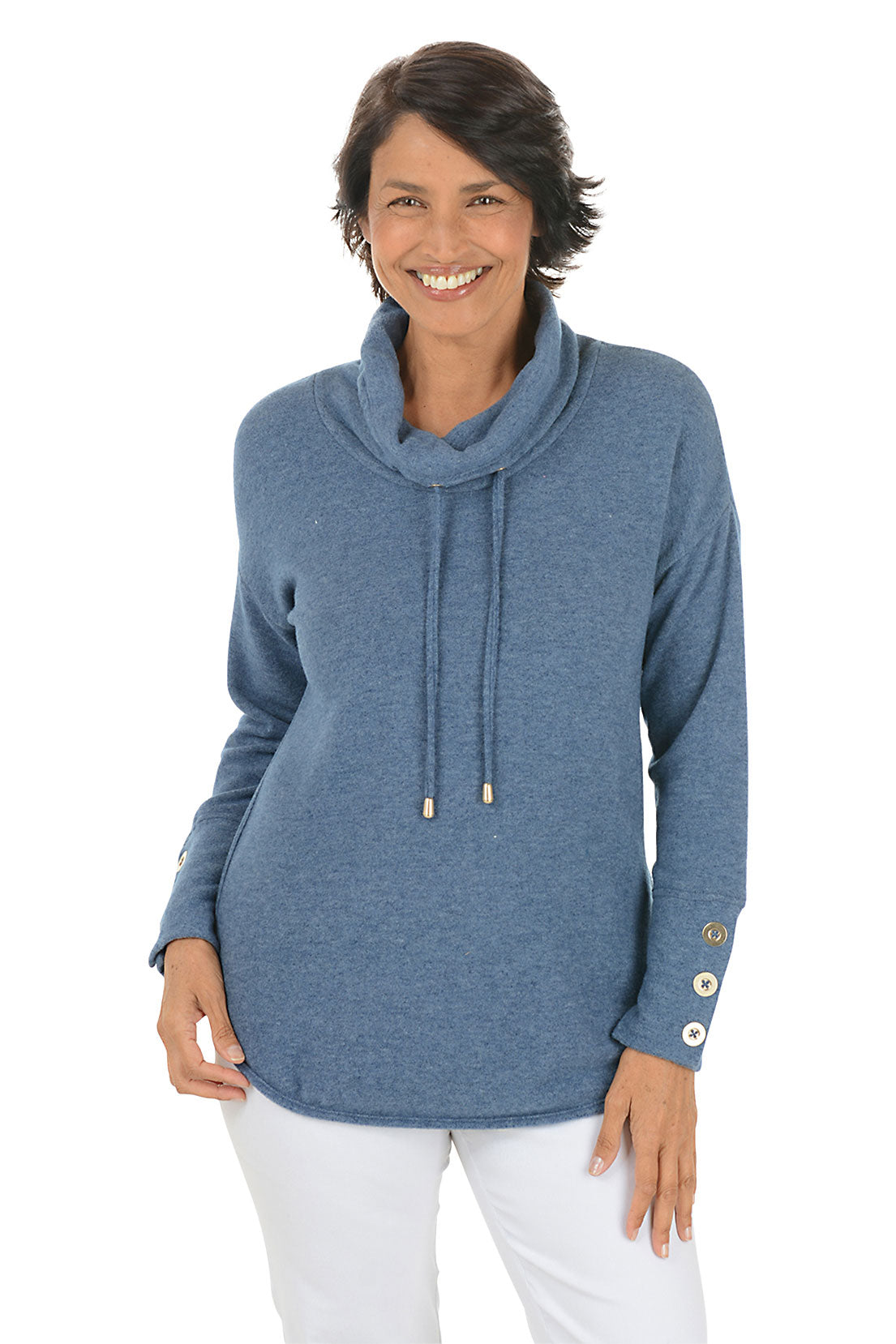 Woman wearing a blue cowl-neck sweater with white pants on a white background.