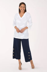Woman wearing a white blouse and navy pants with gold buttons on a white background